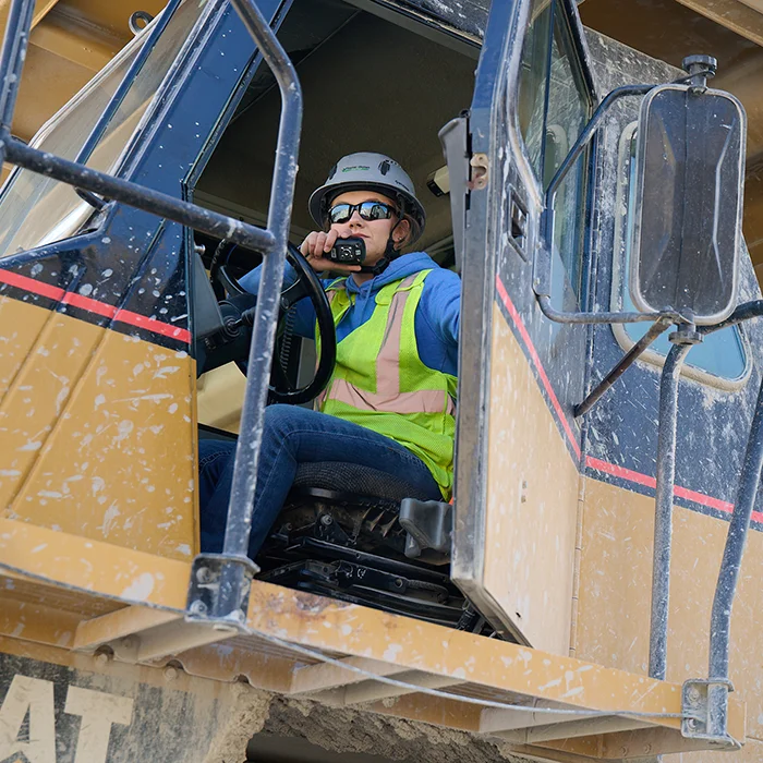 Woman in heavy equipment with the door open talking on a walkie talkie