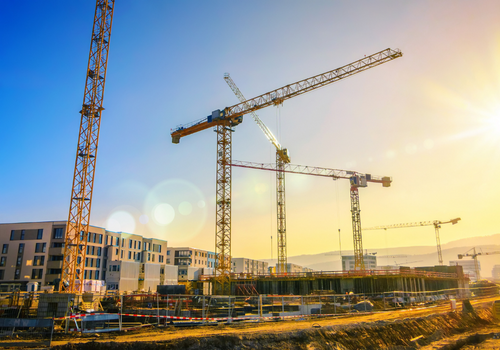 Large construction site including several cranes working on a building complex, with clear blue sky and the sun